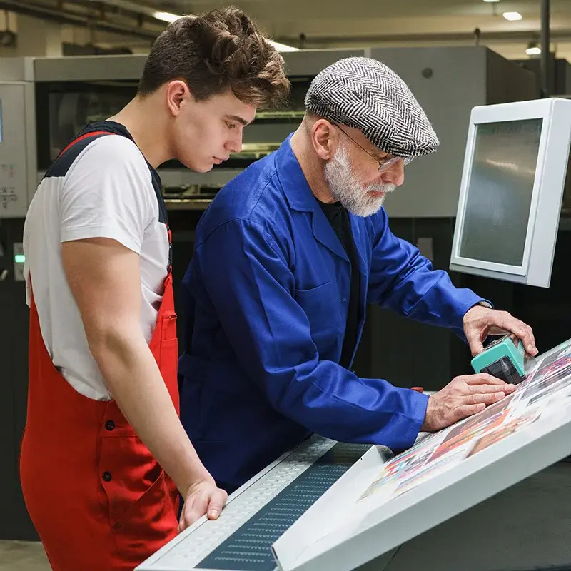 Two print-room workers checking a print proof beside production equipment