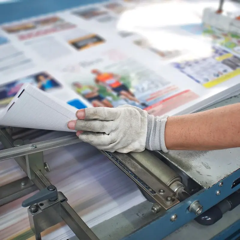 Gloved worker checking or handling a stack of printed sheets